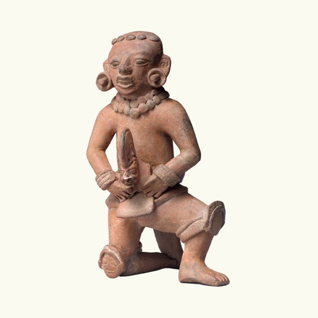 A rust-colored ceramic figure kneeling holding a head or hacha.