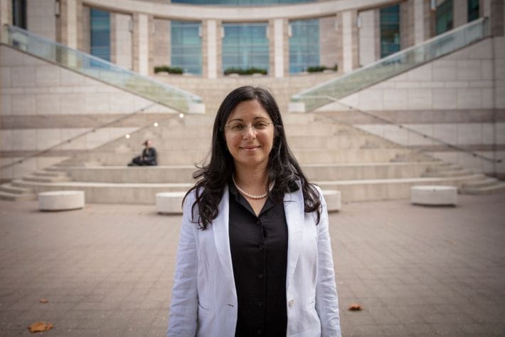 Jeanne Paz stands smiling in her lab coat in front of a building at the Gladstone Institute.