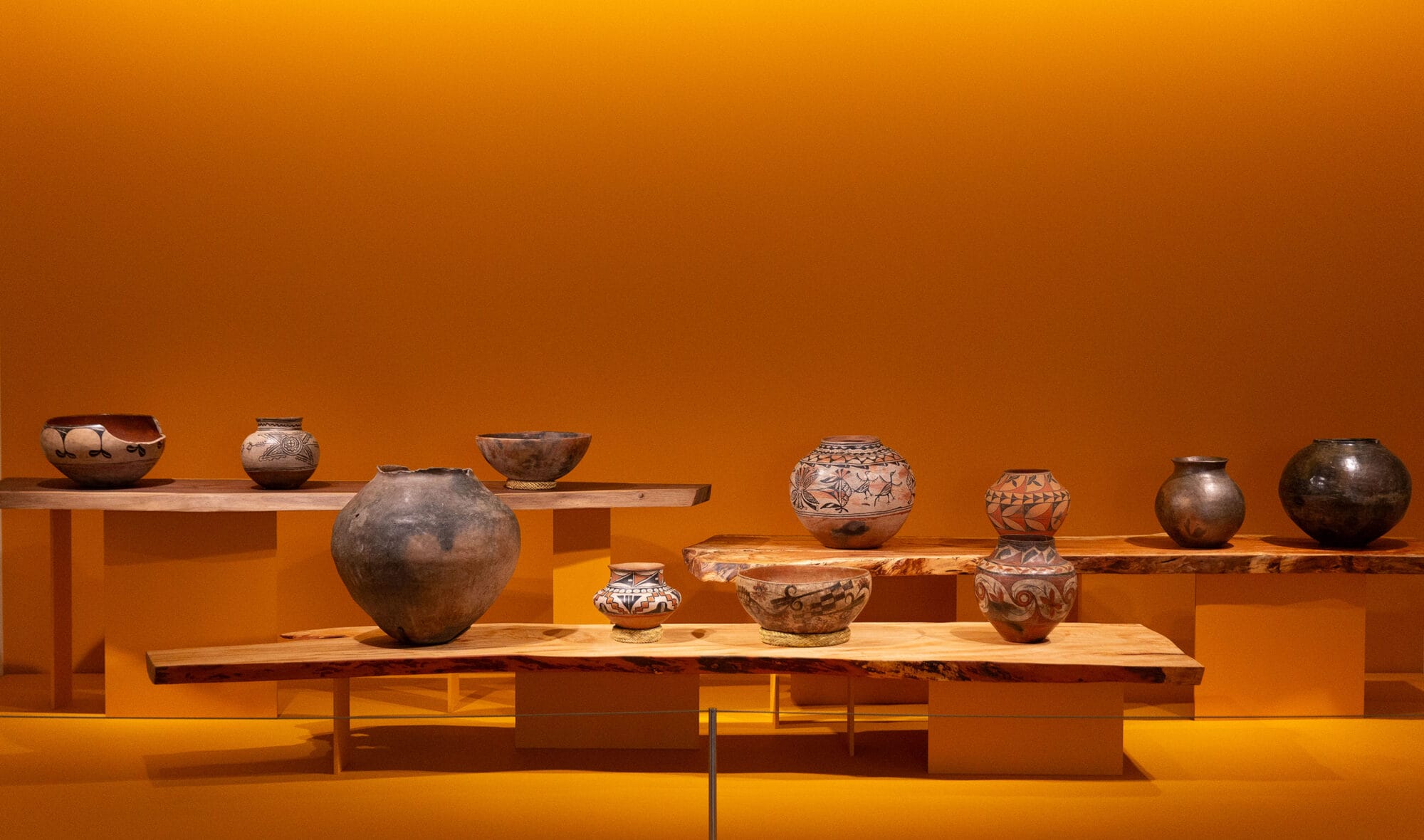 Pueblo Pottery on tables in front of an orange wall.