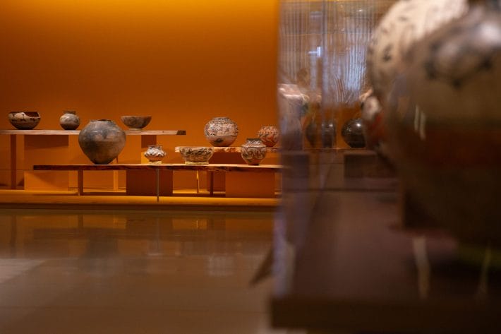 Pueblo pottery placed in cases and on tables in a gallery.