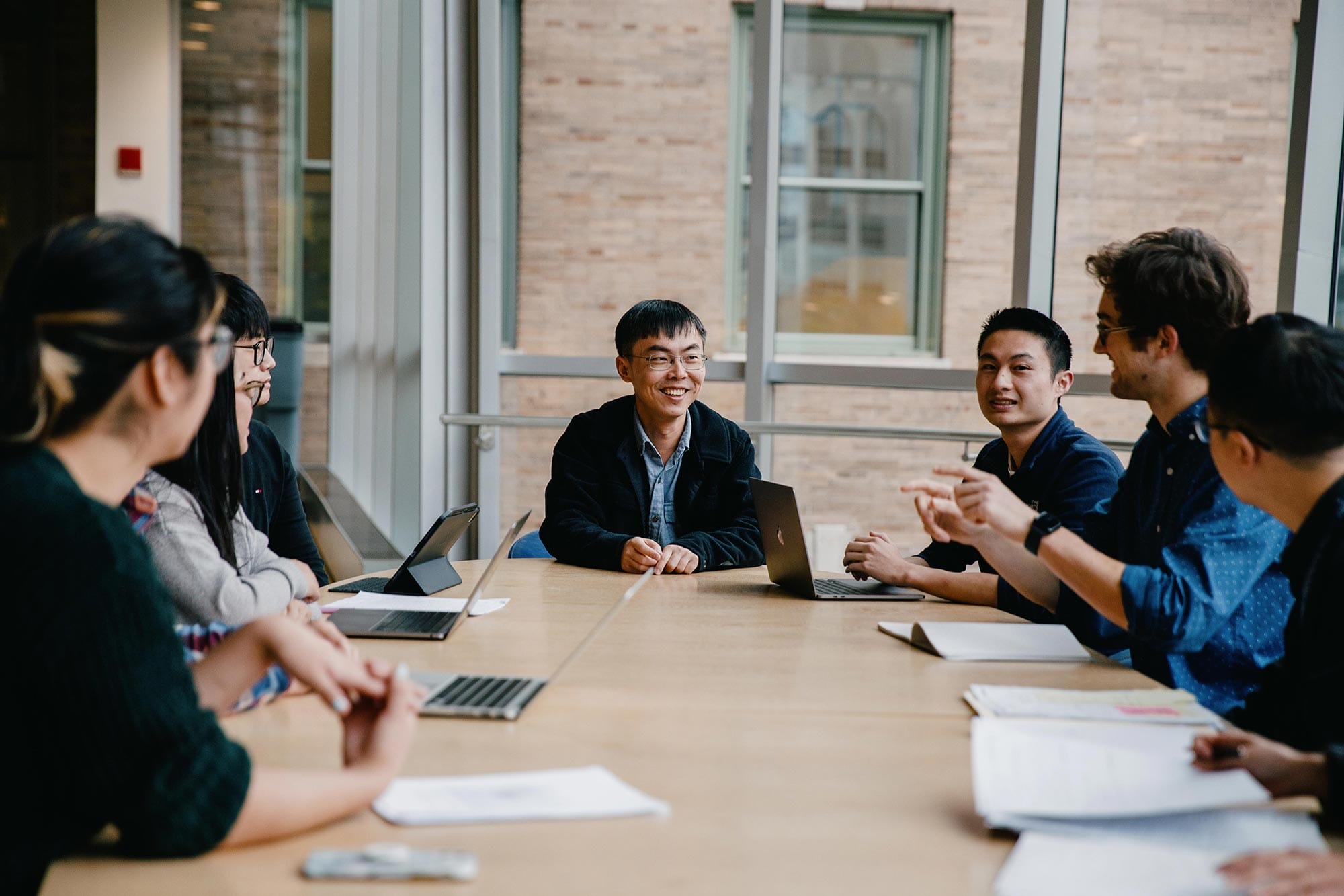 Shixin Liu seated around a conference table with graduate students.