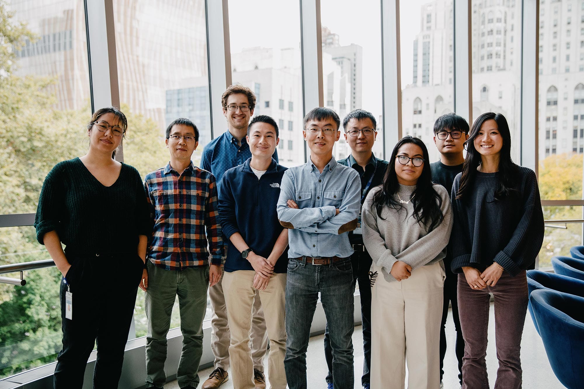 A group photo of Shixin Liu's lab in front of a wall of windows.