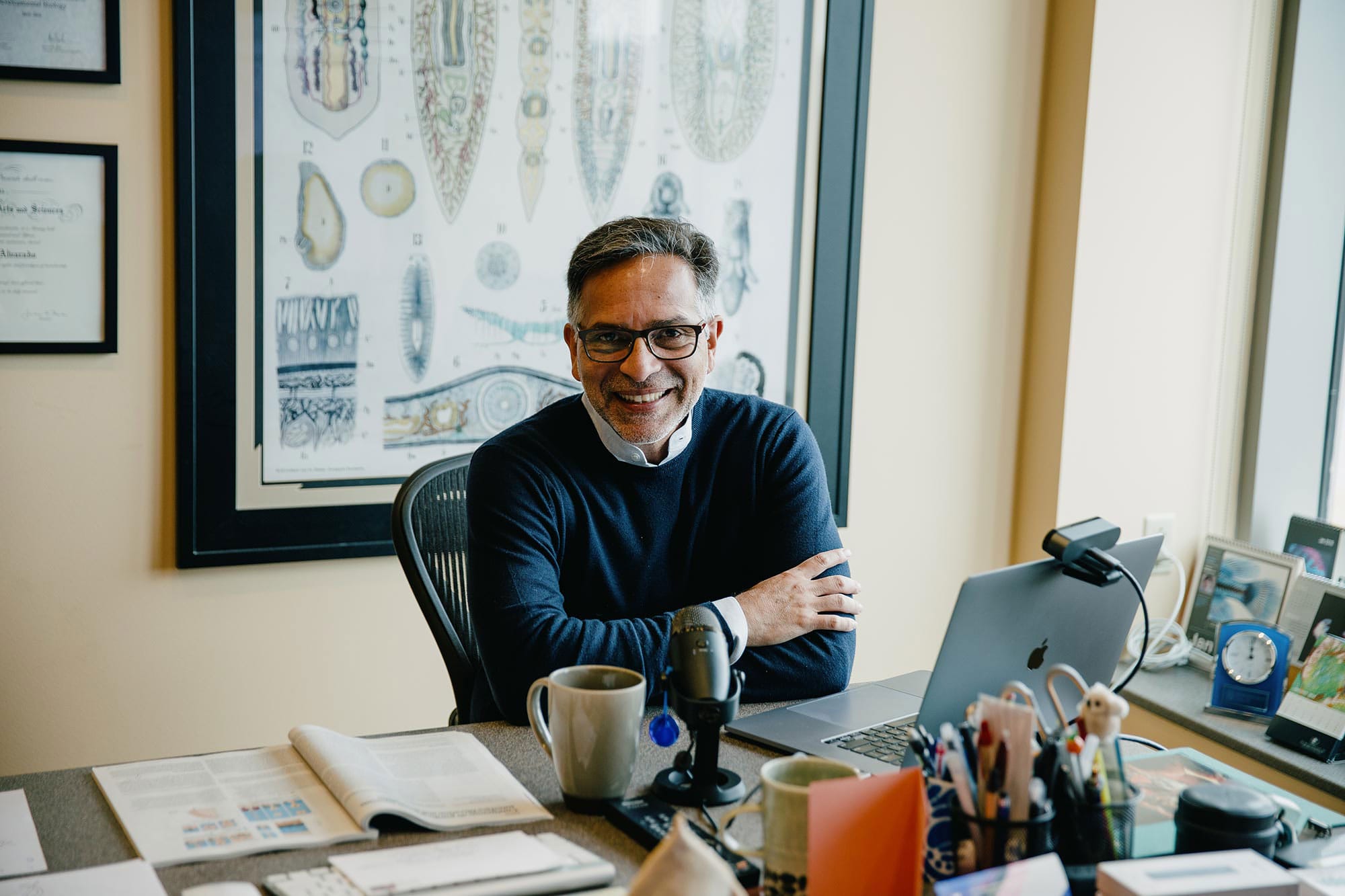 Alejandro Sánchez Alvarado, wearing a navy sweater, sits smiling at his desk.