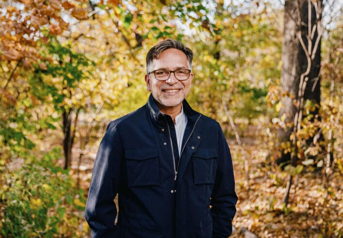 Alejandro Sánchez Alvarado, wearing a navy jacket, stands outdoors between the trees.