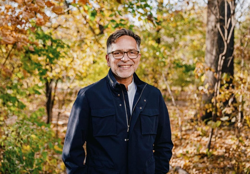 Alejandro Sánchez Alvarado, wearing a navy jacket, stands outdoors between the trees.