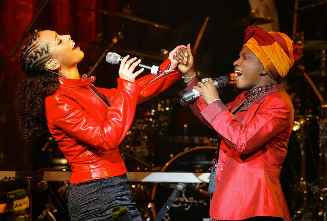 Angélique Kidjo (right) dressed in red singing onstage with Alicia Keys (left).