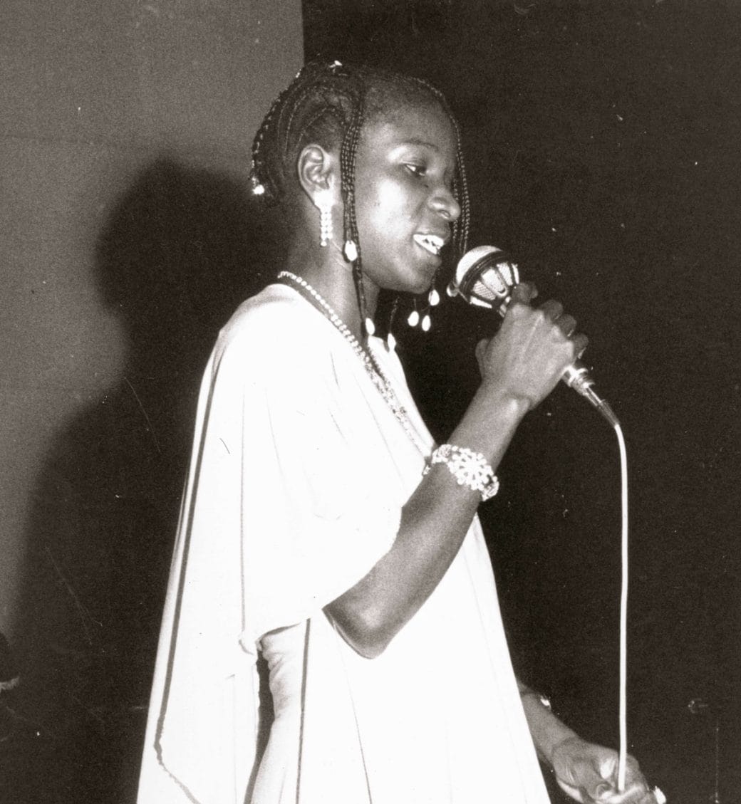 An old black-and-white photo of Angélique Kidjo singing.