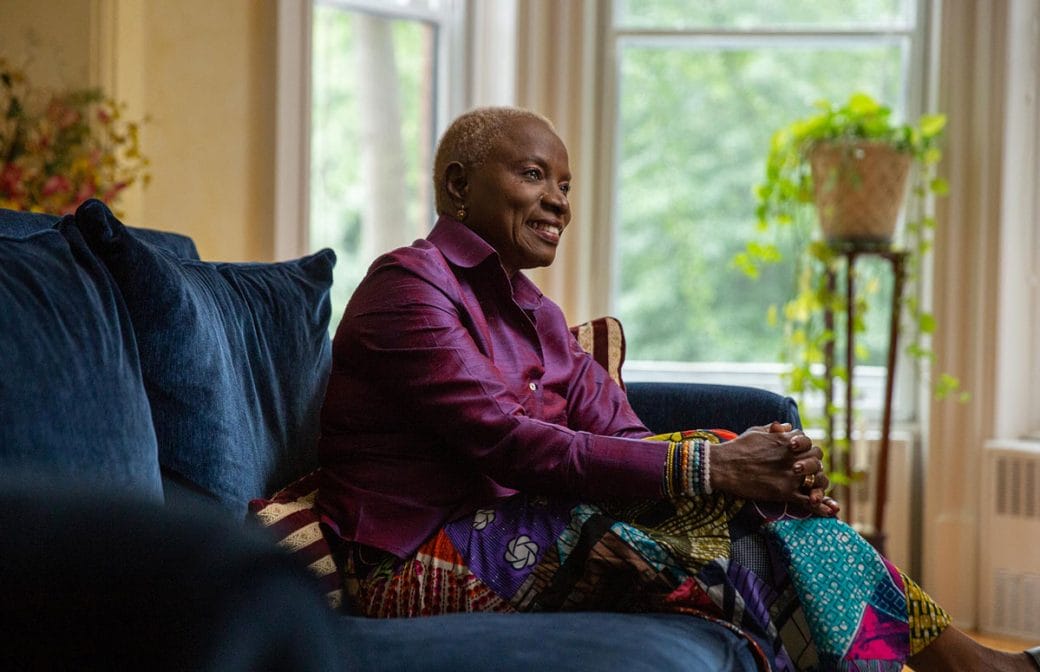 A profile view of Angélique Kidjo sitting on a blue velvet couch.