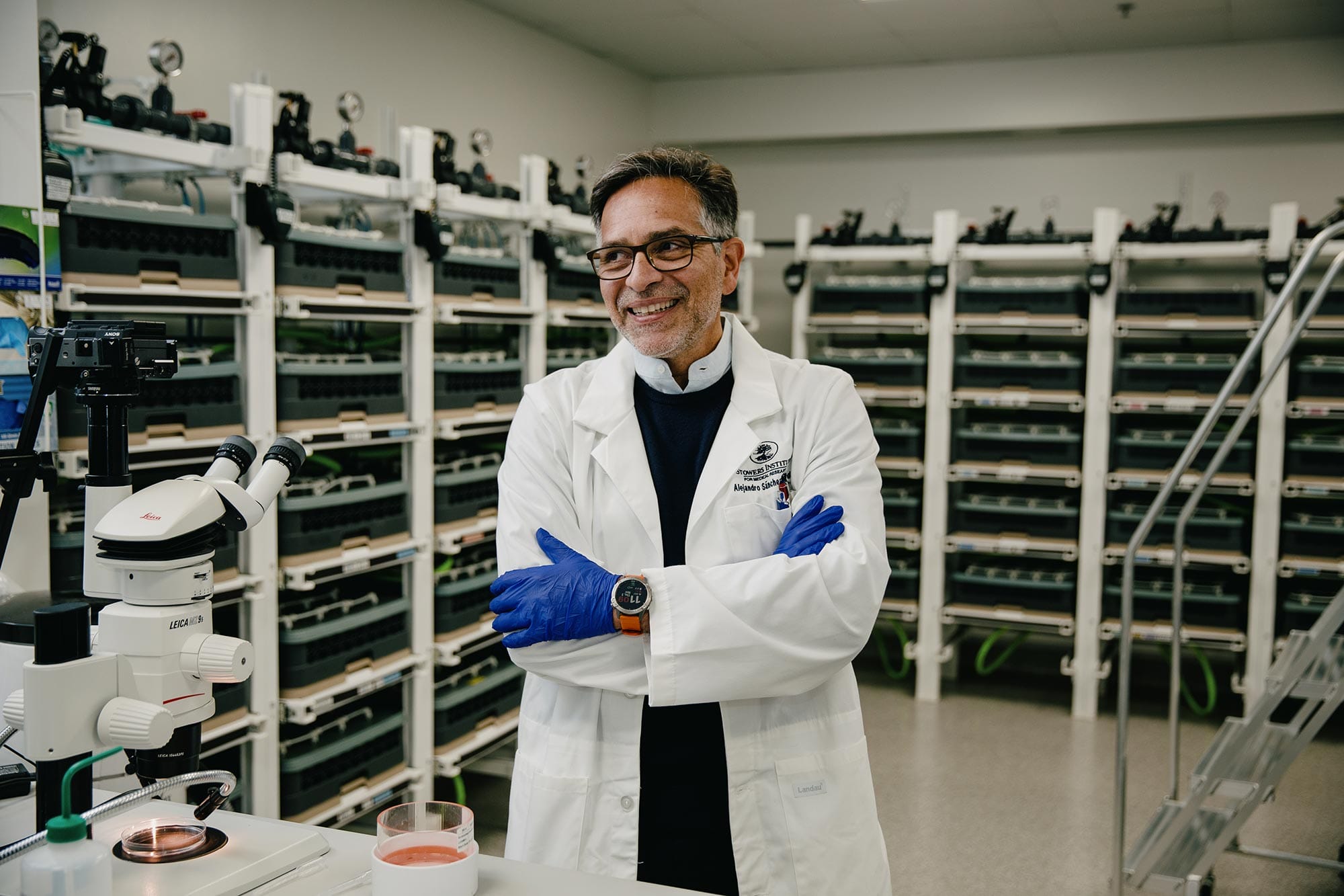Alejandro Sánchez Alvarado wearing a white lab coat, standing in the microscope room at his lab.