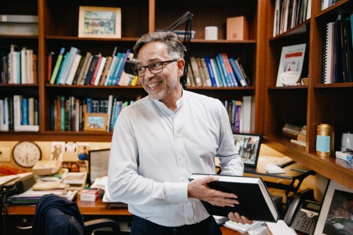 Alejandro Sánchez Alvarado standing in this office holding a black book.