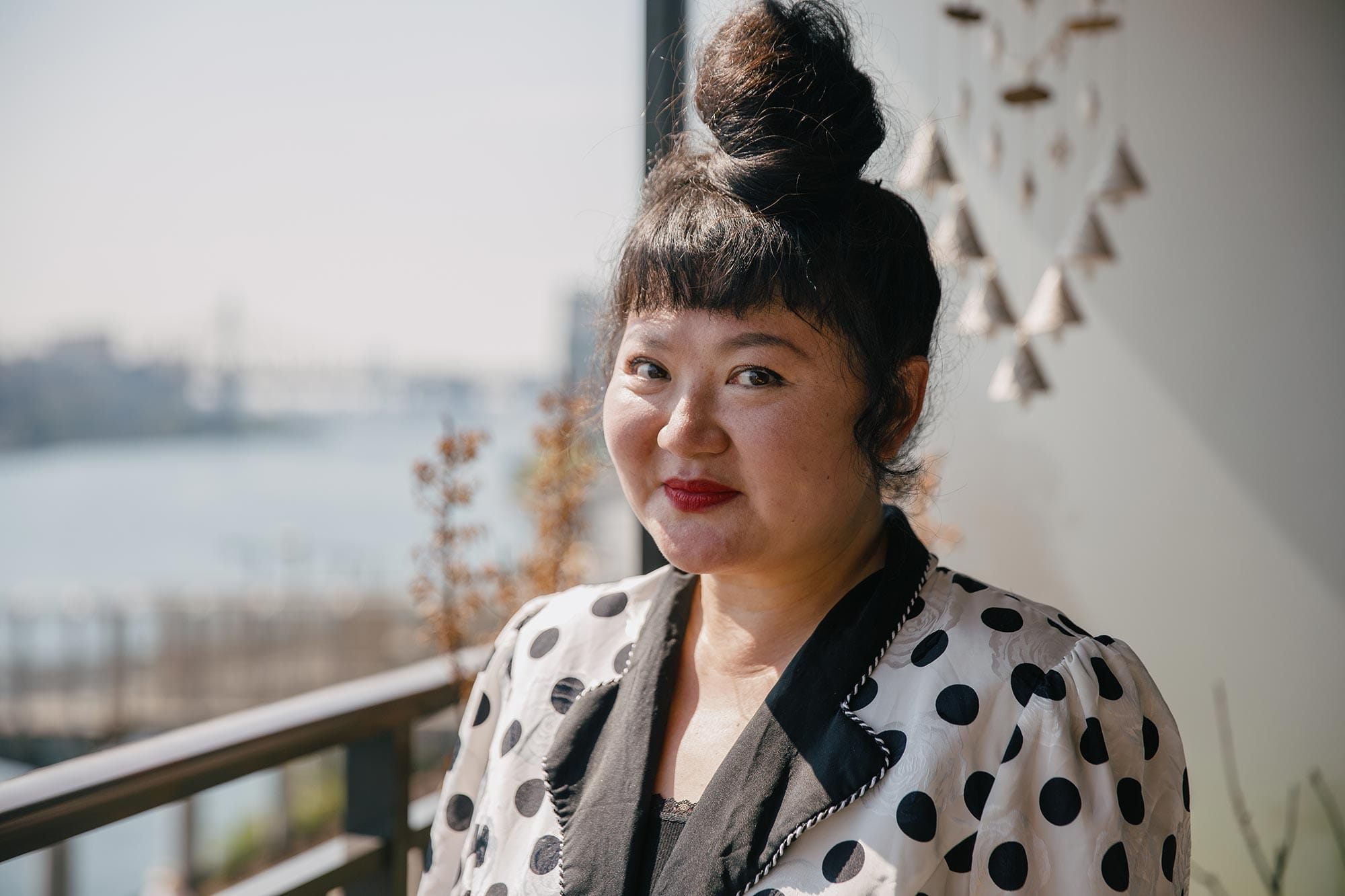 Du Yun wearing a white & black polkadot blazer, standing by a window.