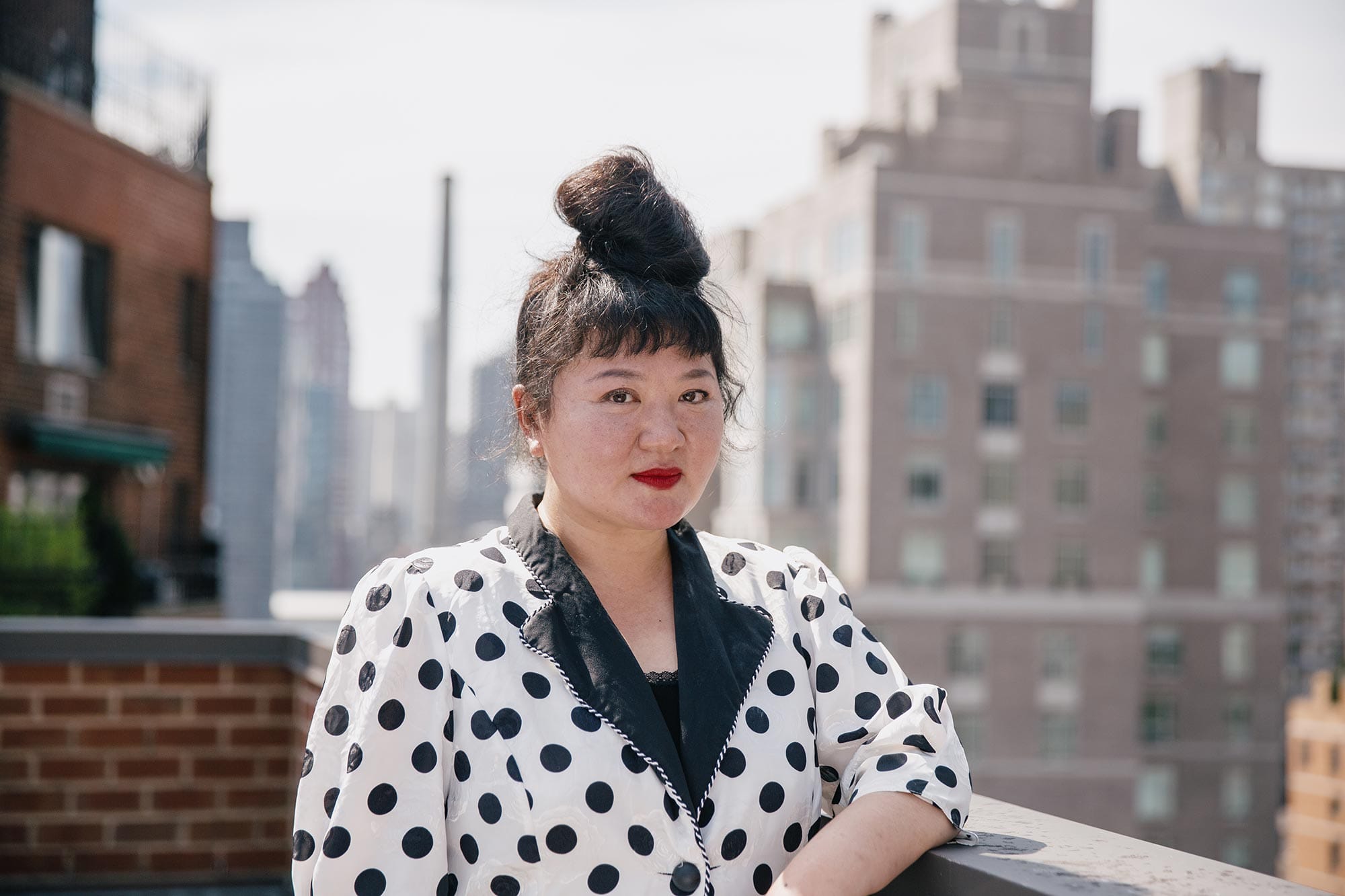 Du Yun in a white & black polkadot blazer with buildings in the background.