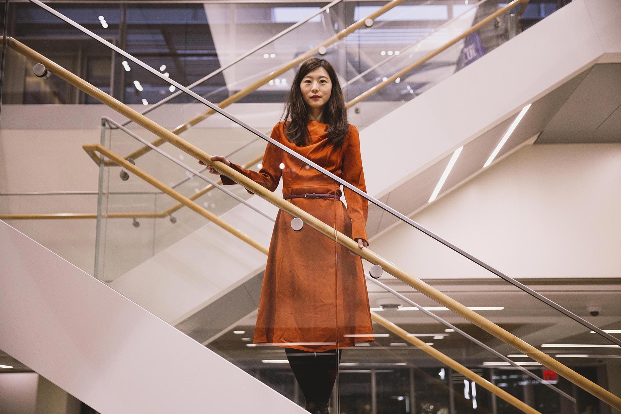 Biyu J. He standing on a staircase with glass railings.