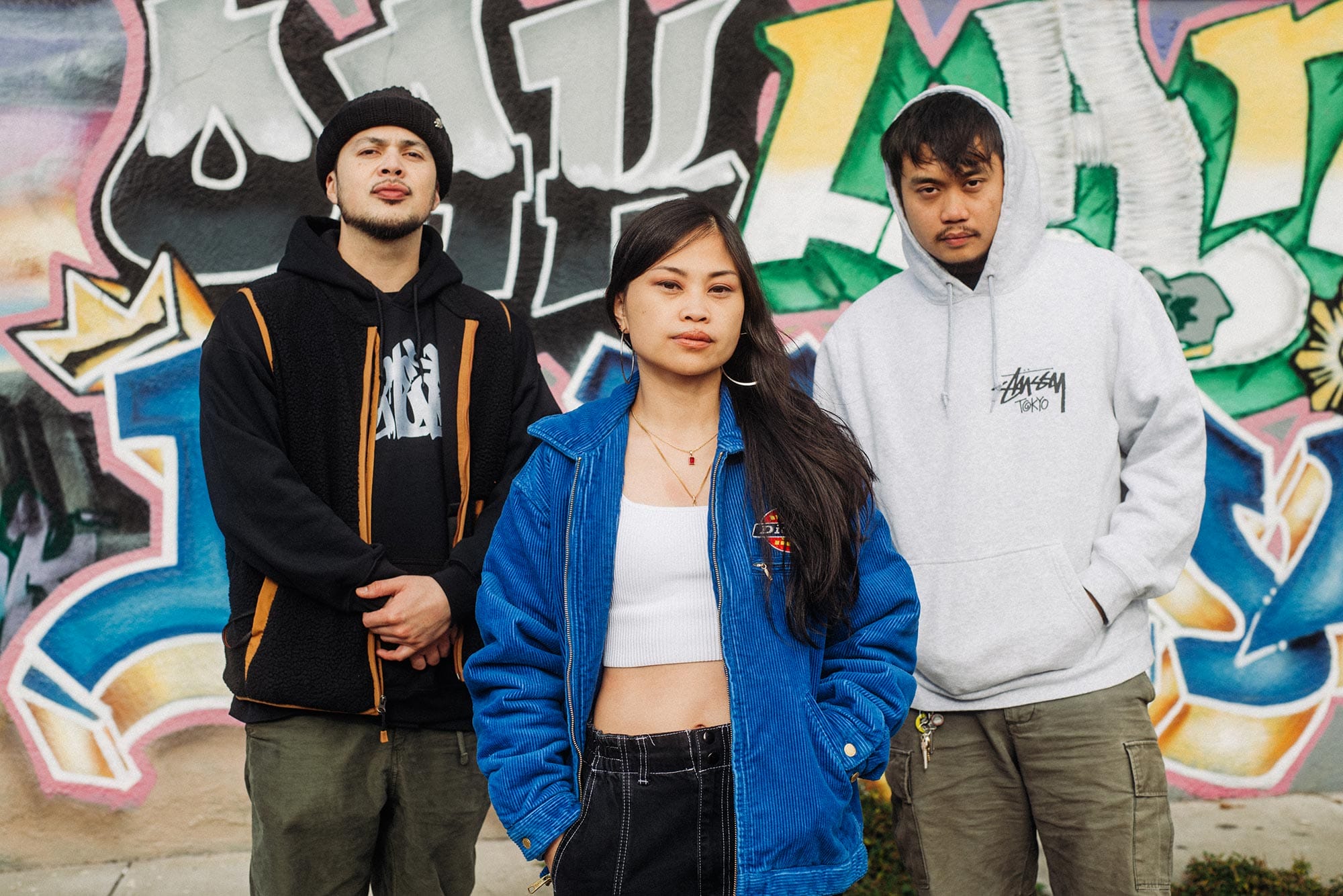 Ruby Ibarra and two of her collaborators in front of a mural with graffiti.