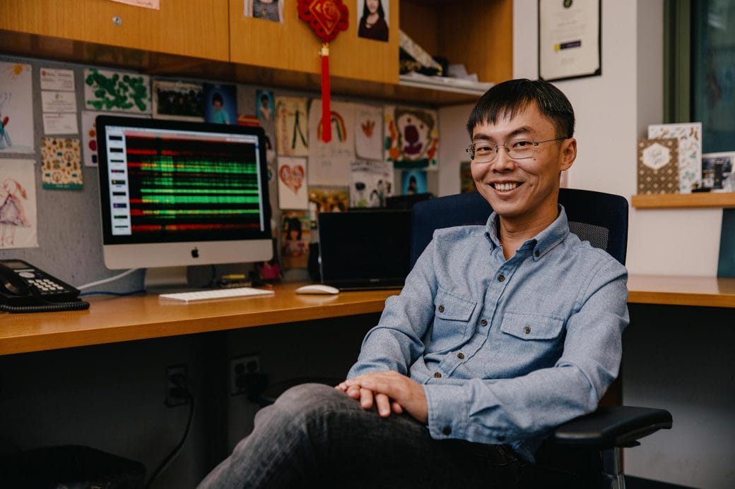 Shixin Liu smiling as he sits in his office.