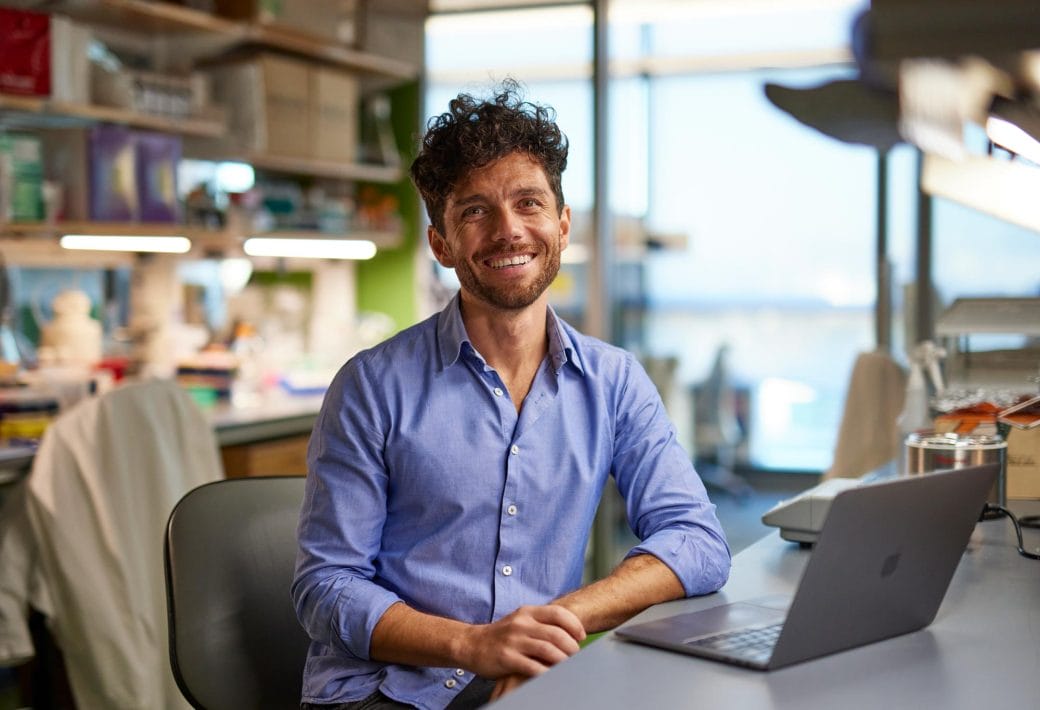 Edward Chouchani smiles behind his laptop in his lab.