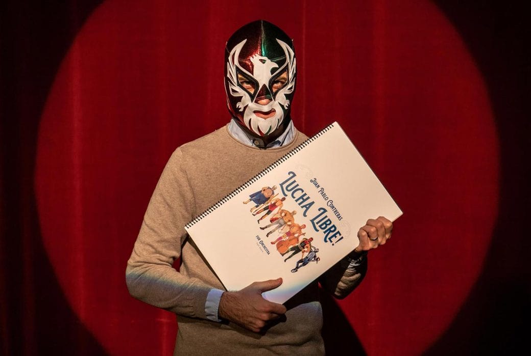 Juan Pablo Contreras wearing a Luche Libre mask holding the sheet music for his composition.