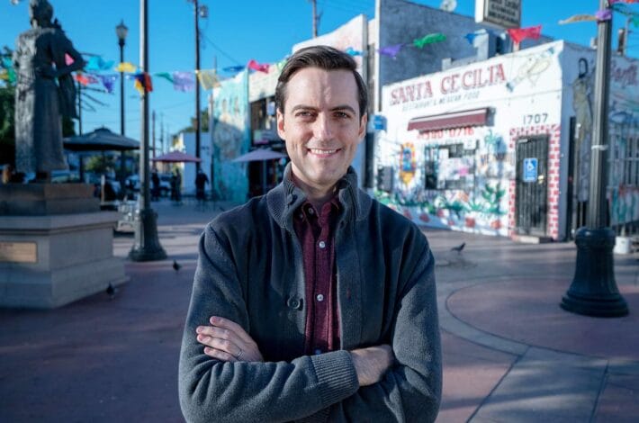 Juan Pablo Contreras stands in a town square with colored flags behind him.