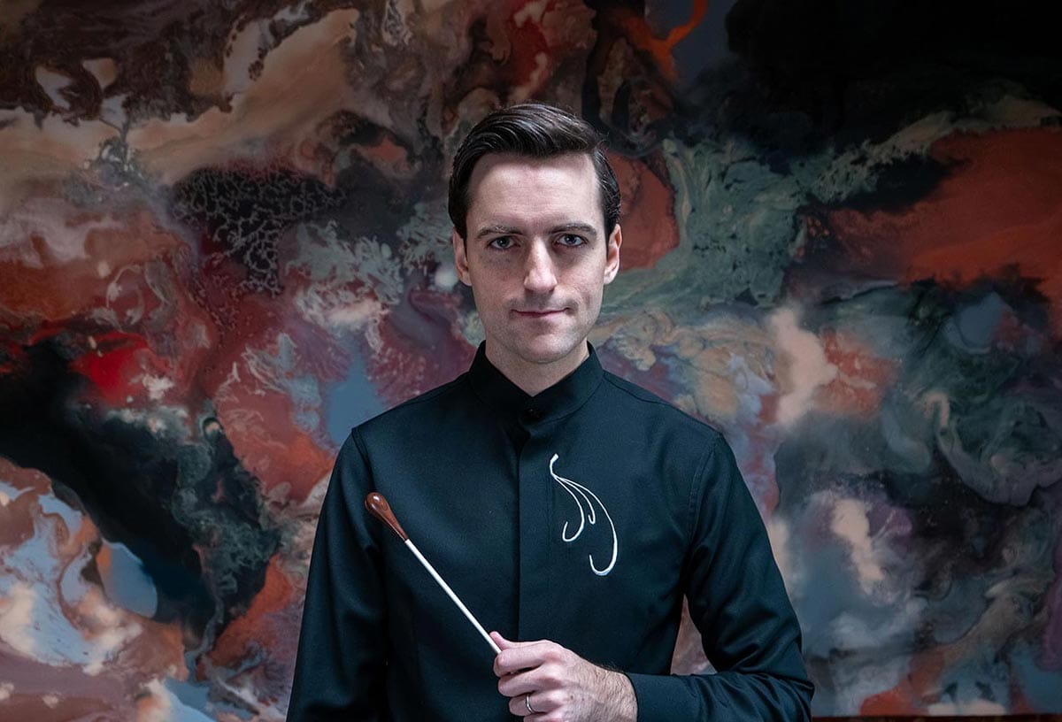 Juan Pablo Contreras poses in the front of an abstract painting holding a conducting baton in his hand.