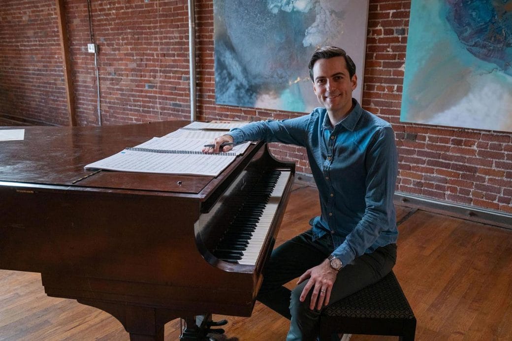 Juan Pablo Contreras seated at a grand piano with sheet music spread out in front of him.