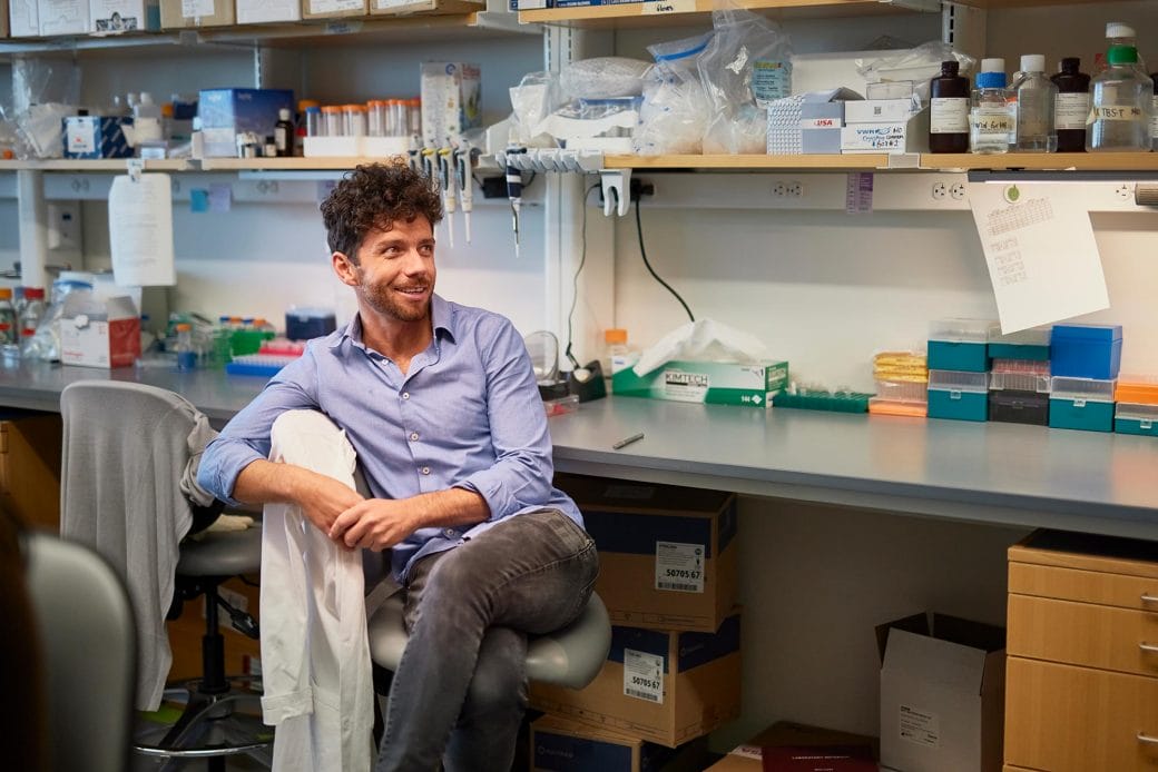 Edward Chouchani sits on a chair with a lab coat draped over the back of it.