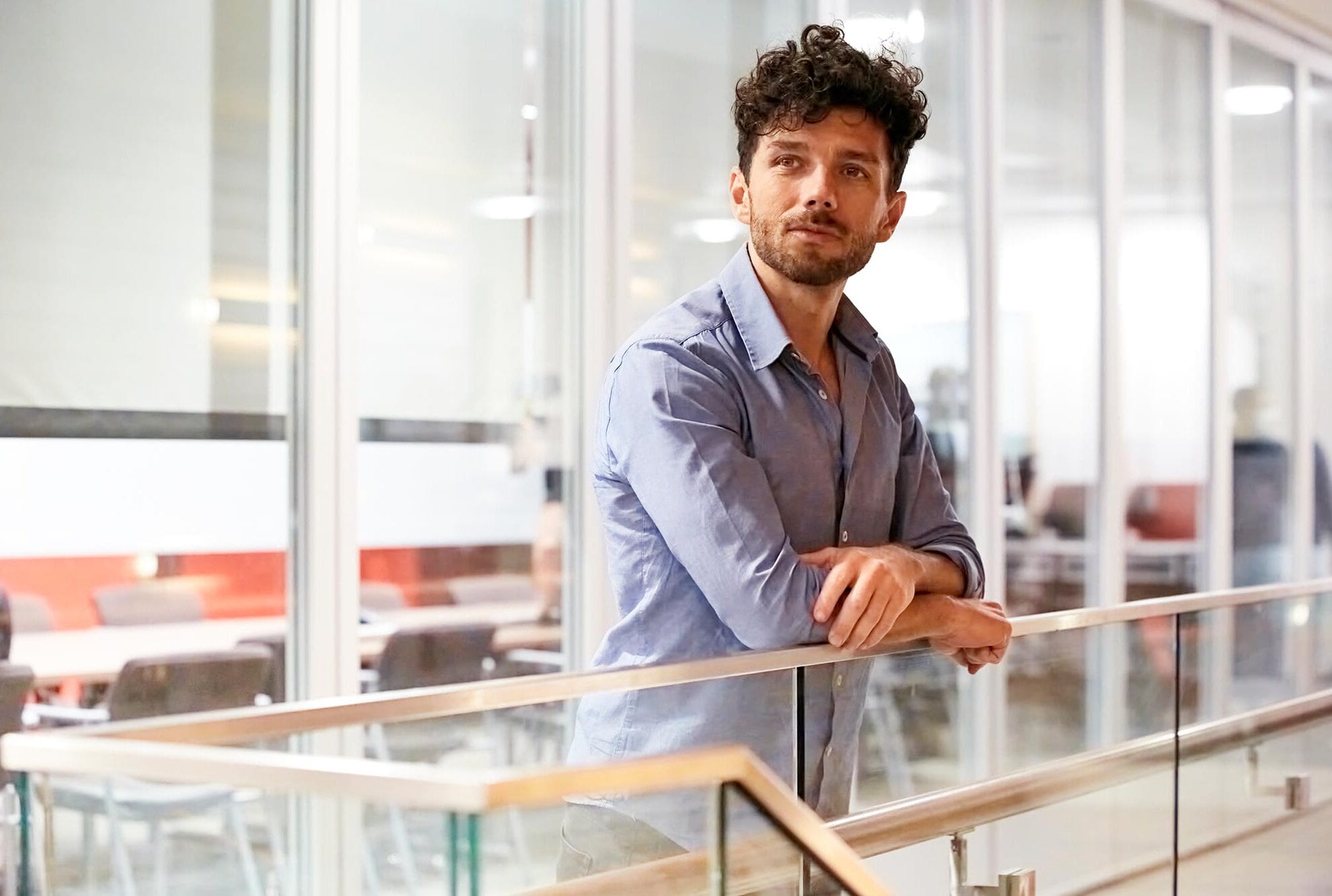 Edward Chouchani leans on a banister in front of a meeting room.