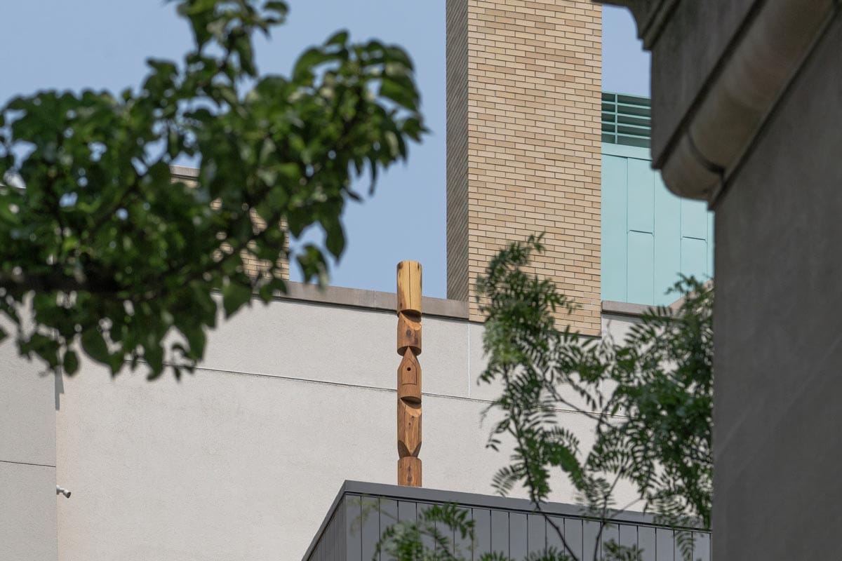 The birdhouse on the roof of the foundation framed by leaves.