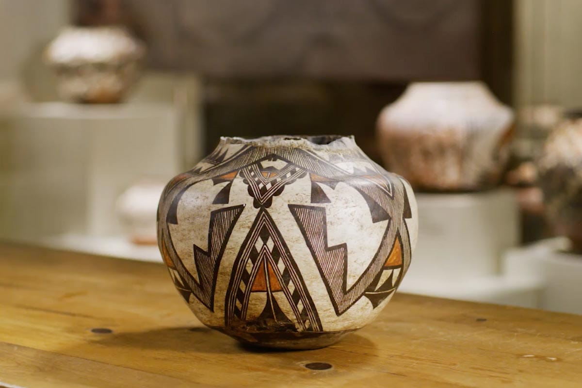 A Zuni pot centered with other pottery works displayed behind it.