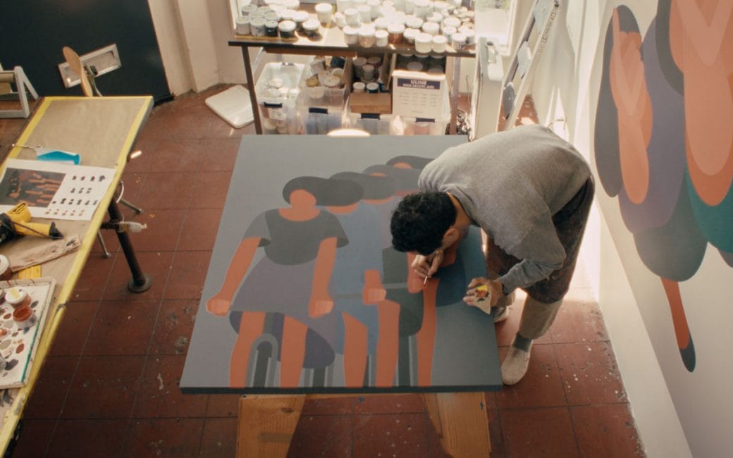 Artist Geoff McFetridge working on a painting in his studio where there are dozens of paint pots.