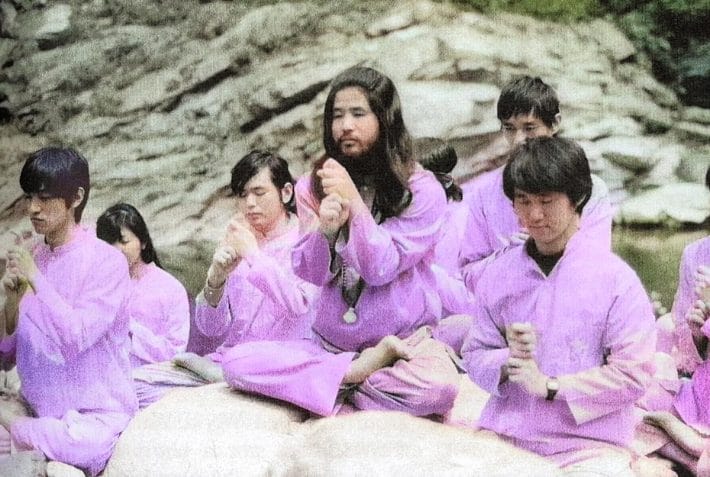 A still of a group of people all dressed in pink garments engaging in symbolic, uniform movement.