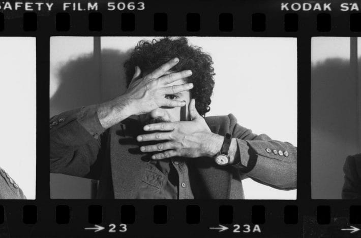 An old reel of film with a man posing with his hands covering his face.