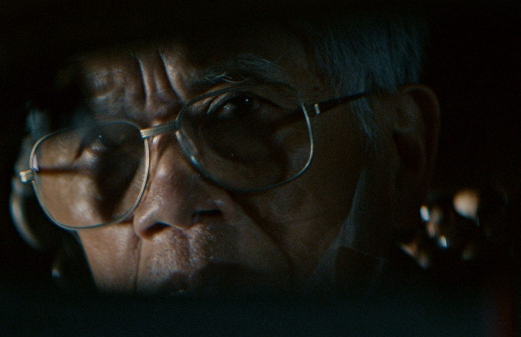 A closeup of taxi driver, Long Má's face as he looks into the taxi's rearview mirror.