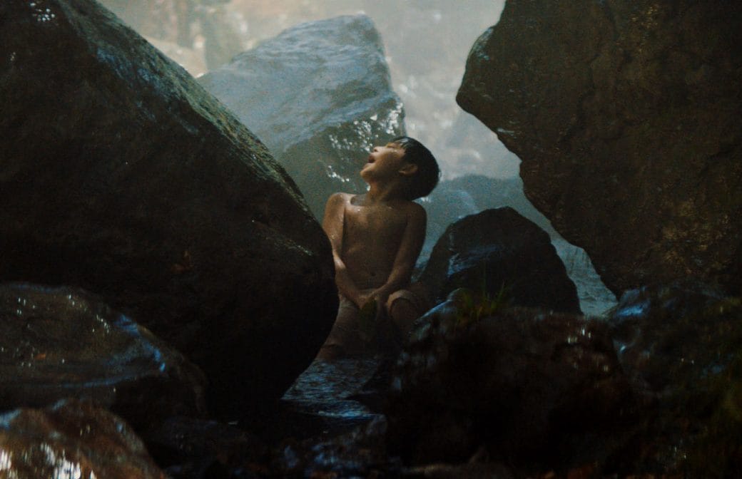 A still of a child sitting on the edge of a rock pool.