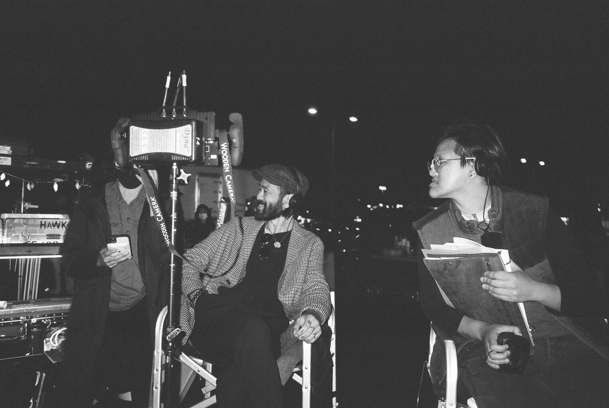 Sing J. Lee sitting in a director's chair on set with a colleague.