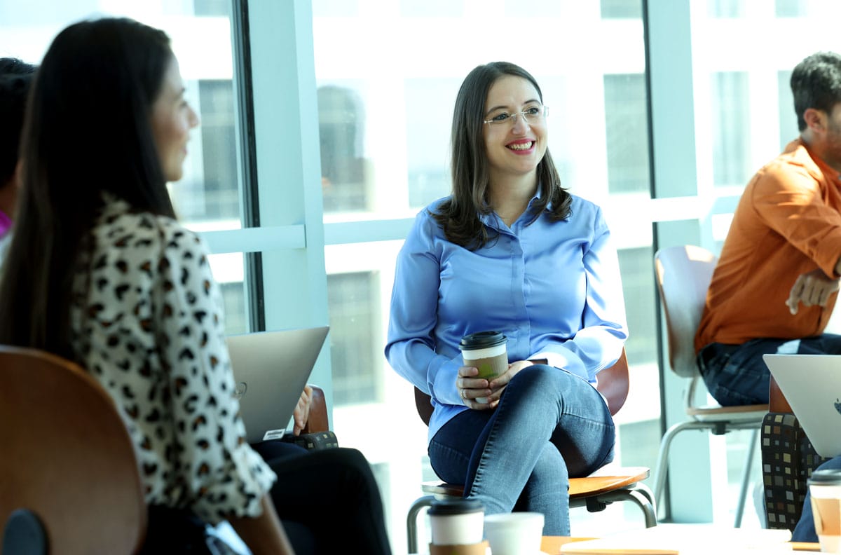 Gerta Hoxhaj sits holding a coffee as she talks with her colleagues.