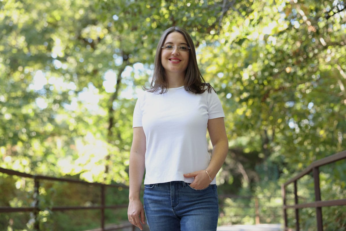 Gerta Hoxhaj walking in a park framed by green leaves.