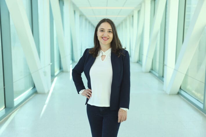 Gerta Hoxhaj standing in a white hallway framed by pillars.