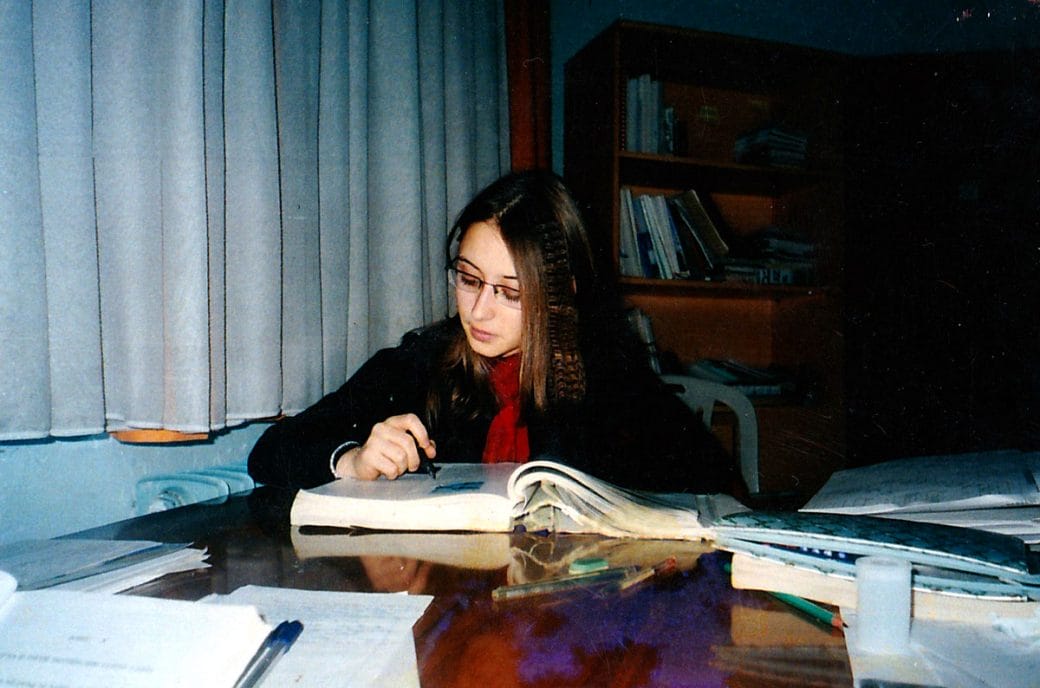 A young Gerta Hoxhaj sits studying a textbook.
