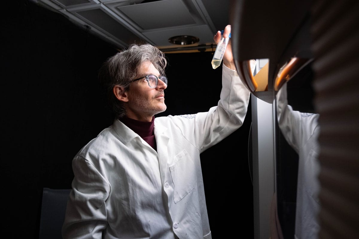 Luciano Marraffini wearing a science lab coat and holding up a vial.