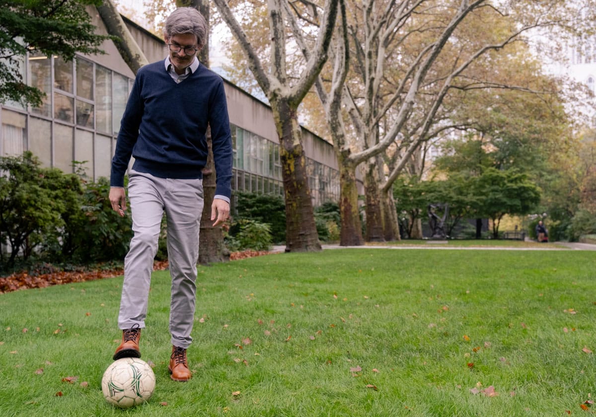 Luciano Marraffini plays with a soccer ball on the grass of an outdoor green space in NYC.
