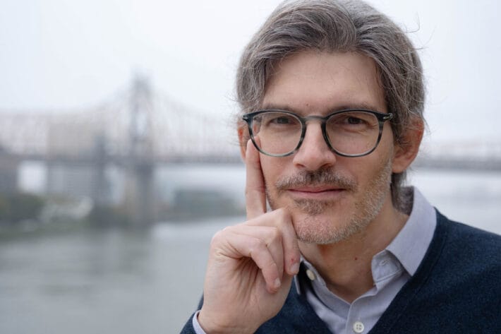 A close up of Luciano Marraffini with an out-of-focus Manhattan bridge behind him.