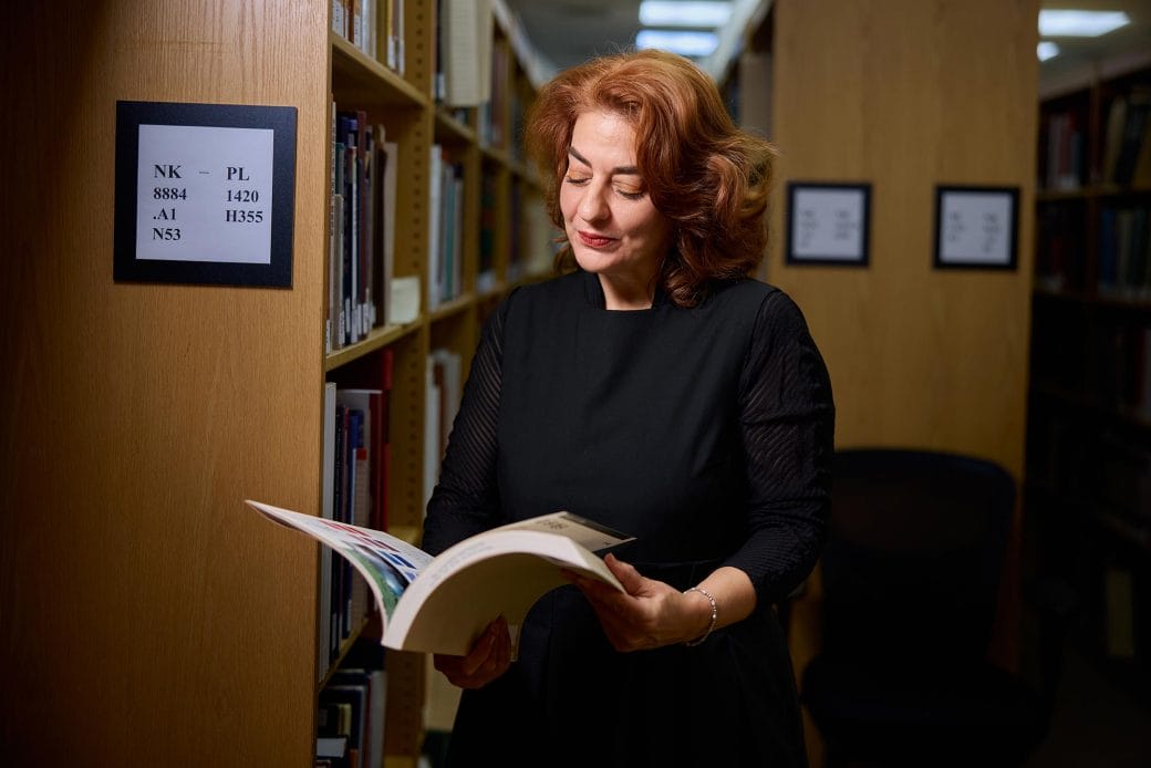 Monika Bincsik standing in front of library racks holding an open book.