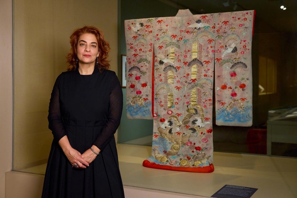 Monika Bincsik standing in front of an art exhibition display case containing a kimono. 