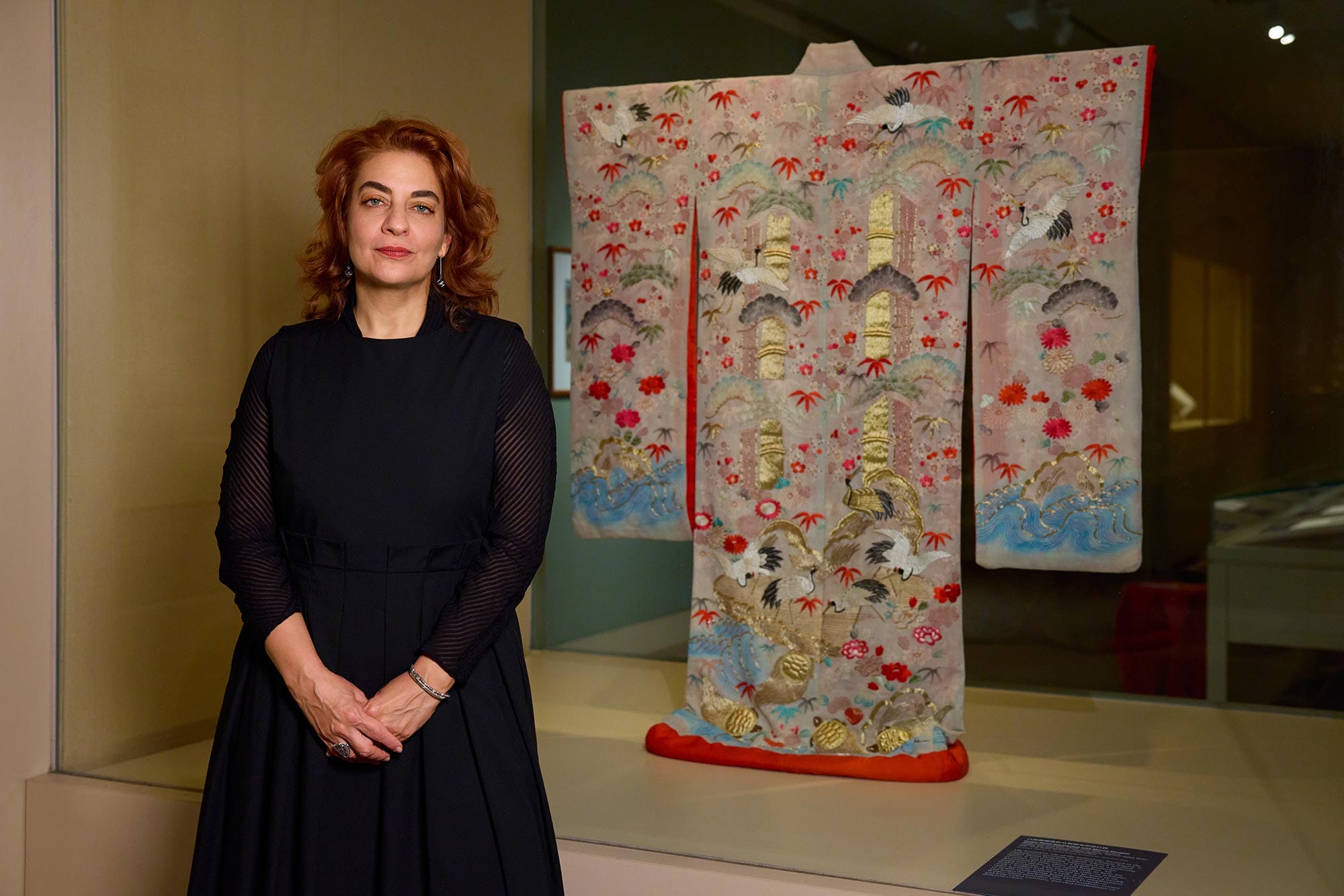 Monika Bincsik standing in front of an art exhibition display case containing a kimono. 