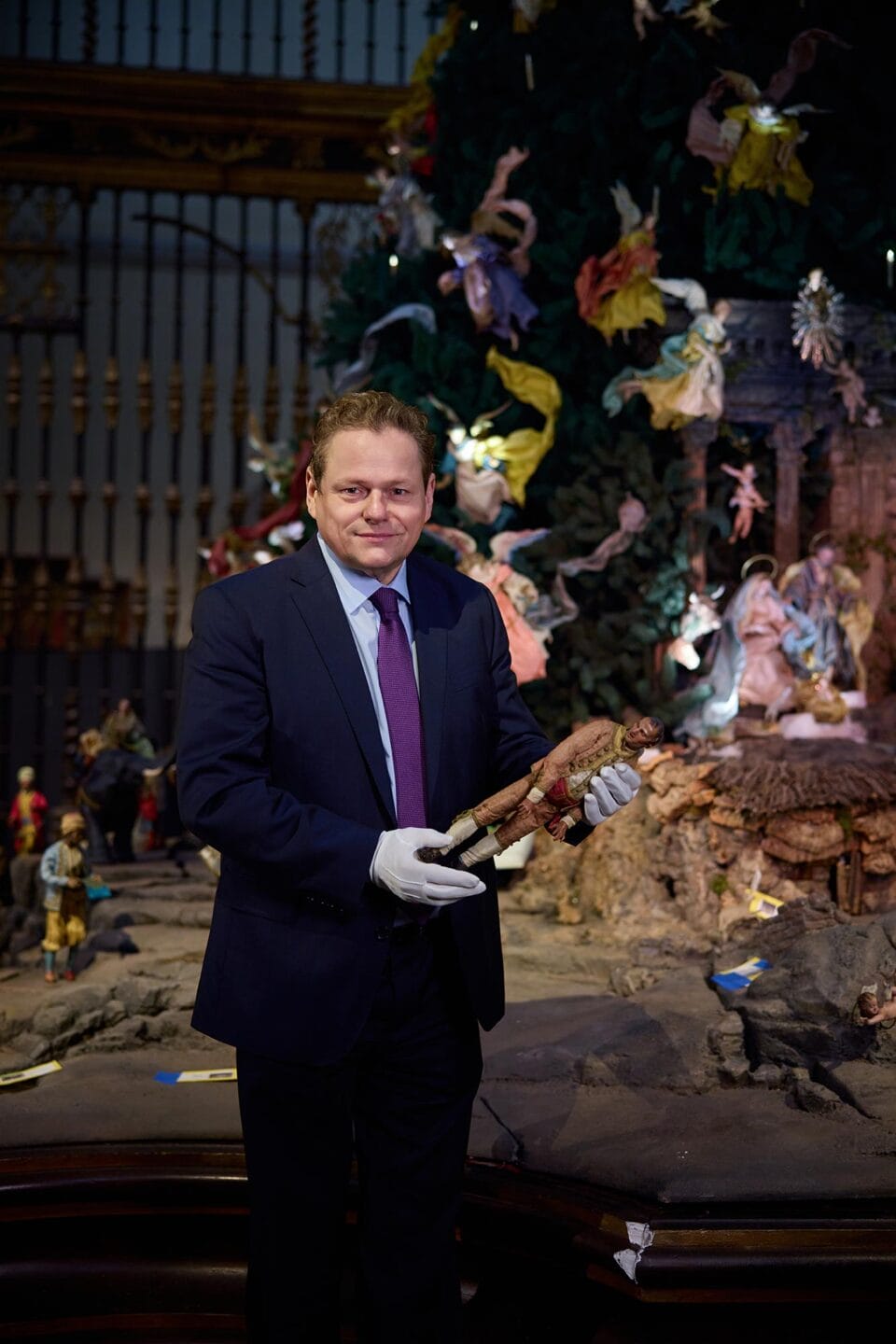 Wolfram Koeppe holding a historical piece from the Neapolitan Baroque Crèche and the Christmas Tree at The Met.