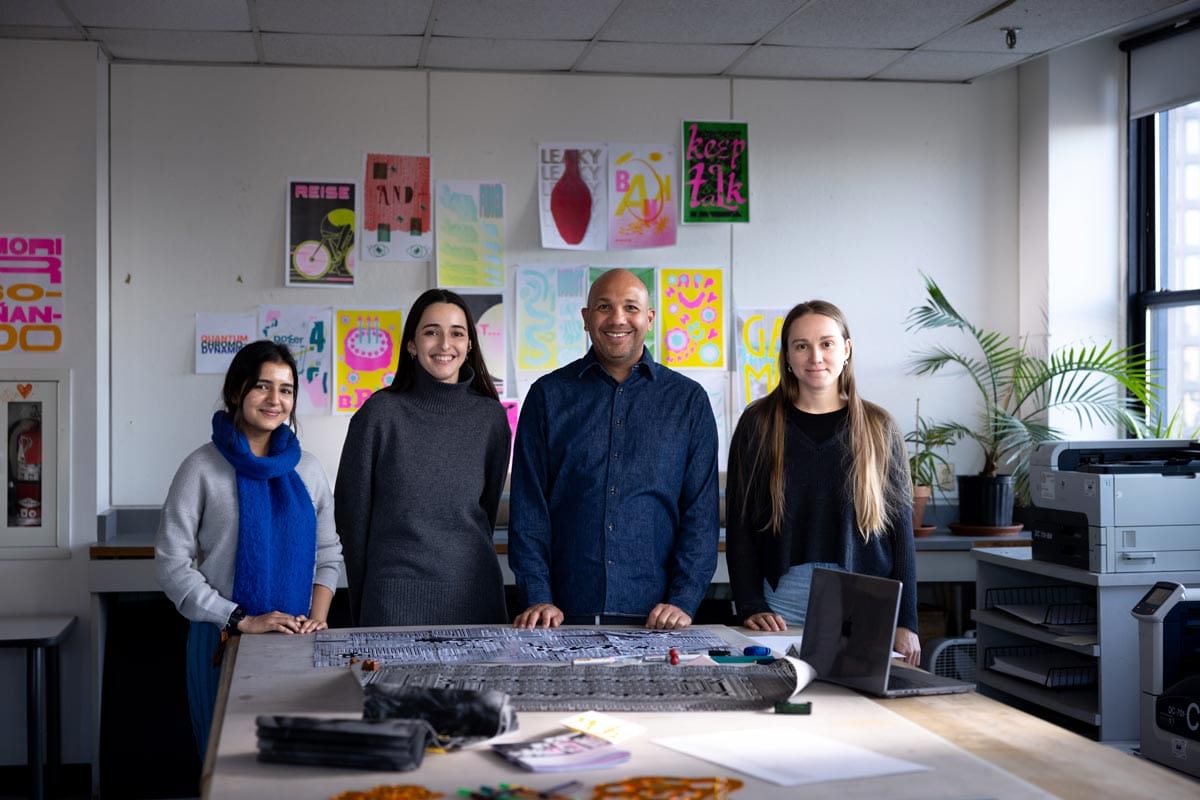 Ramon Tejada smiles alongside three of his students as they work at a large table. 