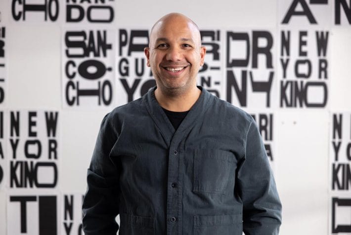 Ramon Tejada standing in front of a wall displaying his typography designs.