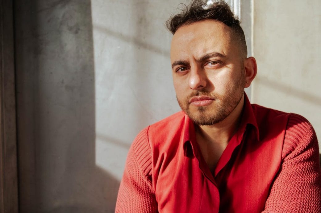 Wael Morcos wearing a red button-down shirt and sitting in front of a gray concrete wall.
