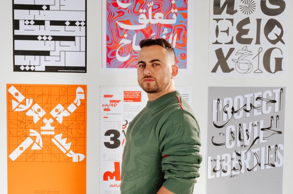 Wael Morcos stands in front a wall with filled with posters of his typographical designs. 