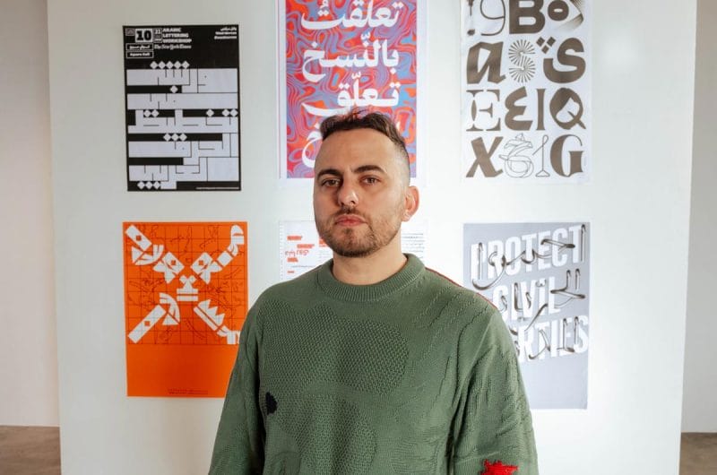Wael Morcos stands in front a wall with filled with posters of his typographical designs.